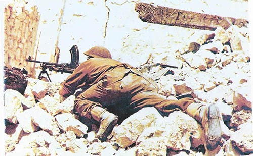 Sgt Carr 1st Somerset Light Infantry using Bren gun in the ruins of Cassino town. (Note the hole in right boot!)